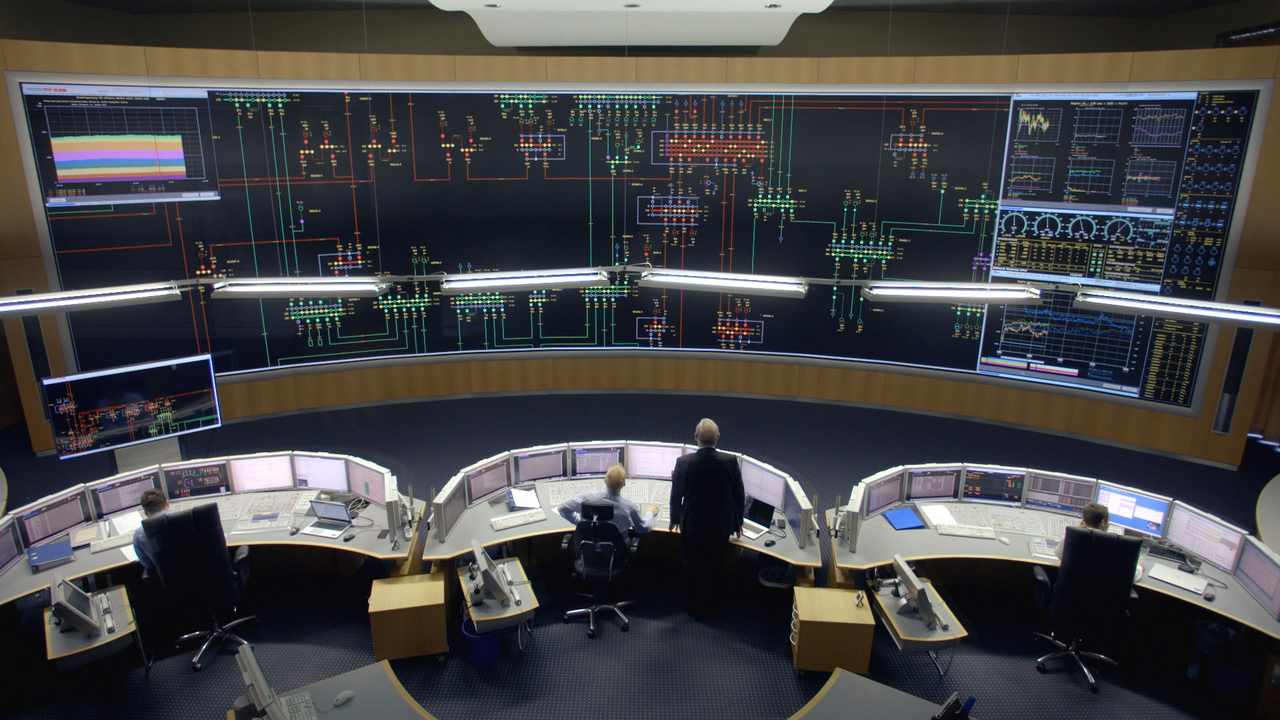 Blick in die Schaltzentrale eines Kraftwerks. An drei halbrunden Arbeitsplätzen sitzen Menschen an Computern. In ihrer Blickrichtung ist eine raumumfassende Anzeige aller Systeme.