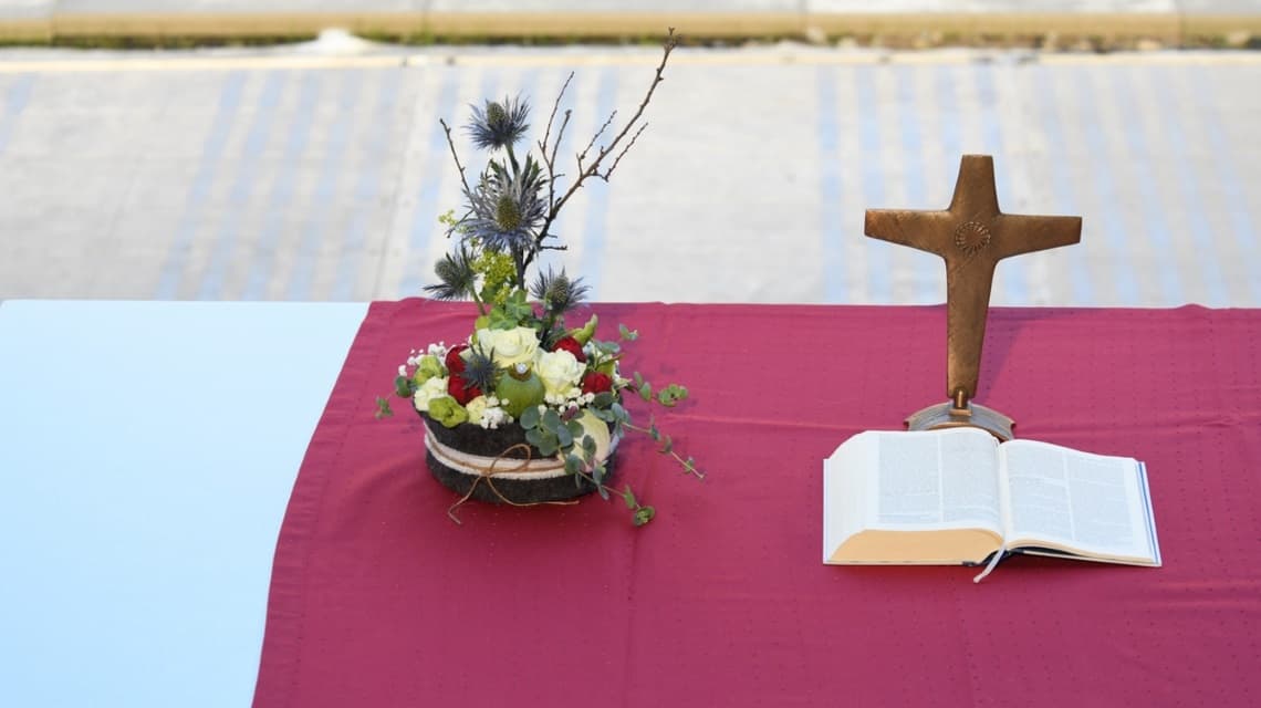 Altar mit Blumengedeck, kupfernem Kreuz und aufgeschlagener Bibel auf einem roten Tuch