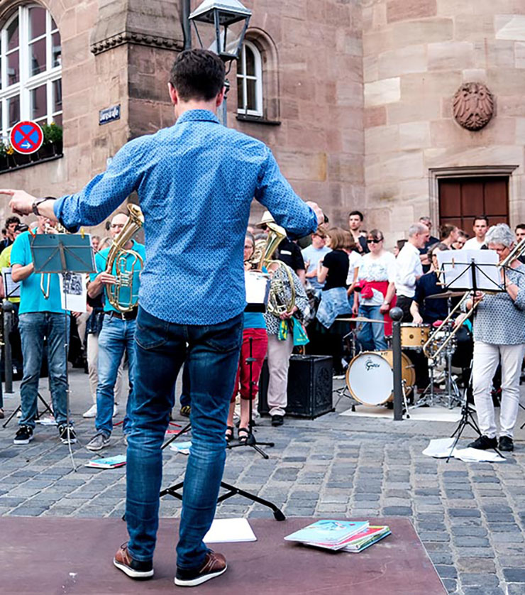 Ein Dirigent auf den Straßen Nürnbergs, vor ihm stehen Musizierende und Zuschauer