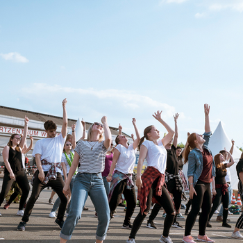 Jugendliche tanzen eine Choreographie und recken den linken Arm in den blauen Himmel beim Kirchentag 2019 in Dortmund 