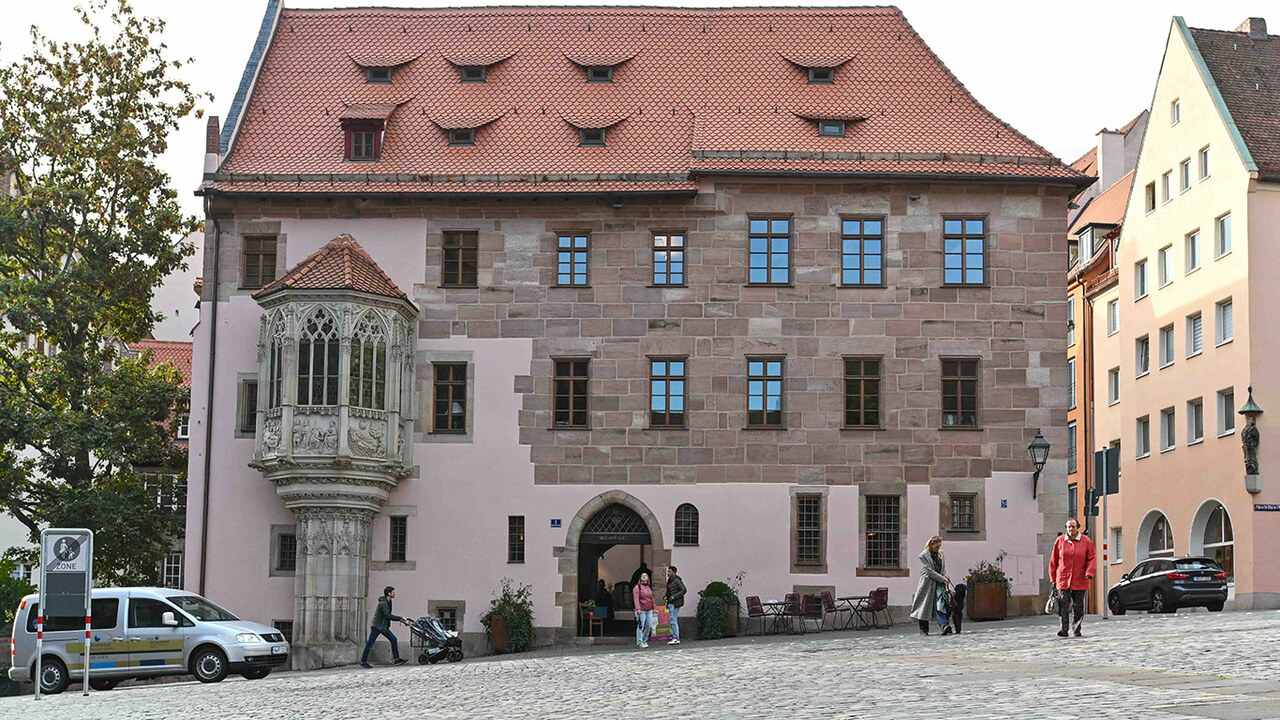 Blick auf das Gebäude des Sebalder Pfarrhofs. Im Vordergrund Laufen Personen über den großen, gepflasterten Vorplatz