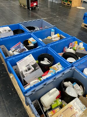 offene, gepackte Kisten stehen in einem Lager, darin: Kannen, Eimer, Cookies, Tee, Ordner und vieles mehr