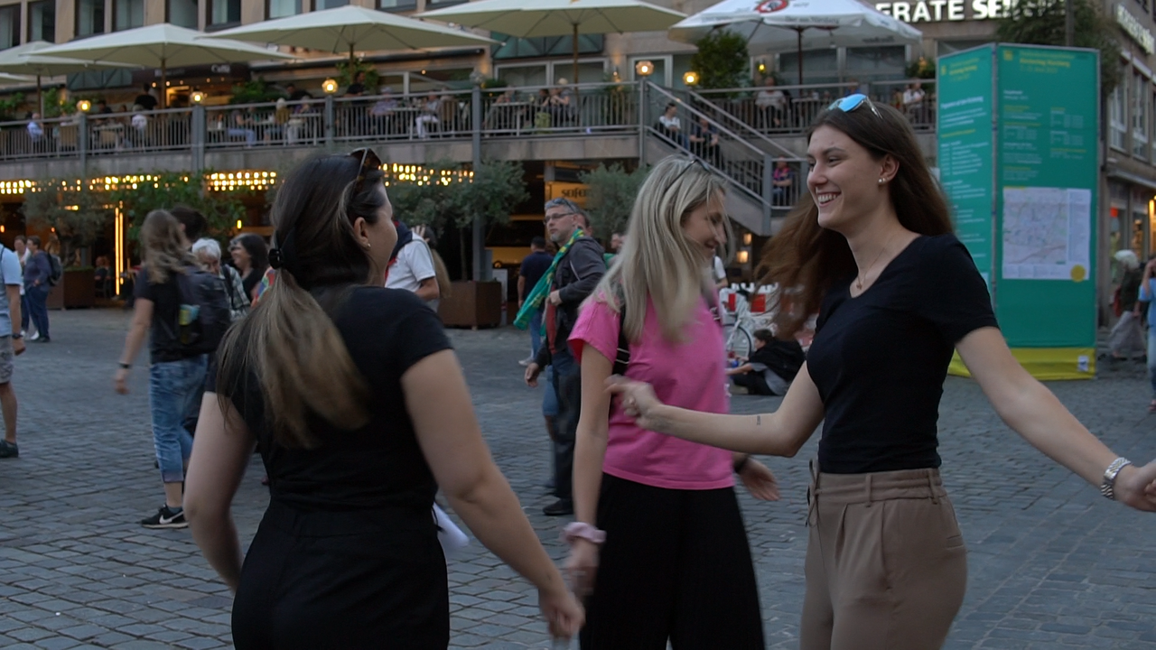 Drei junge Frauen auf einem Platz, die im Kreis tanzen 