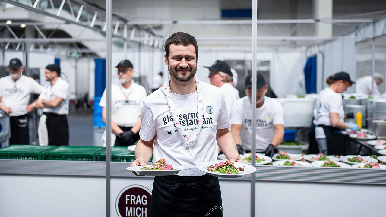 Beim Gläsernen Restaurant 2025 Ein Koch präsentiert zwei Teller mit Gerichten aus dem Gläsernen Restaurant