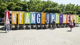 Komposttoiletten, die Türen sind farbig und darauf steht ein großer Buchstabe, so dass sich zusammen ein Regenbogen mit dem Spruch "Anfang und Wende" ergibt