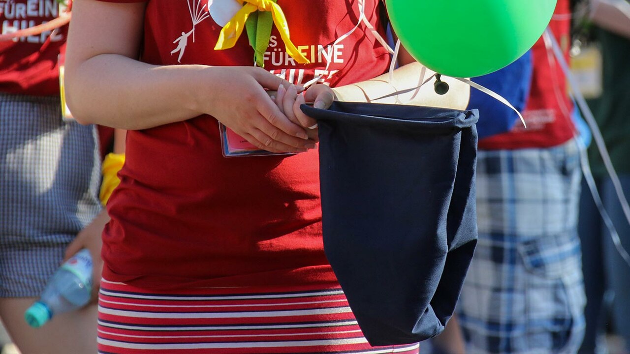 Frau mit rotem Tshirt hält Kollektenbeutel in der Hand