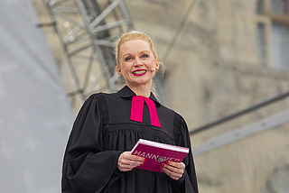 Pfarrerin spricht beim Schlussgottesdienst und hält ein Programmheft