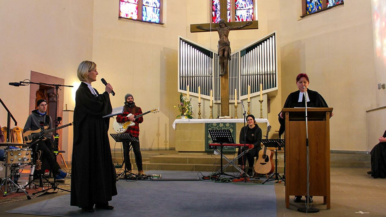 Altarraum mit Band im Hintergrund. Im Vordergrund zwei Frauen bei einer Ansprache (mit Abstand)