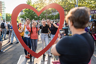 Besucherinnen posieren in einem herzförmigen Rahmen beim Abend der Begegnung