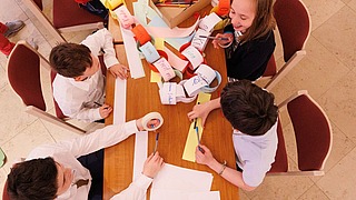 Kinder basteln gemeinsam an einem Projekt und schreiben auf Papierstreifen