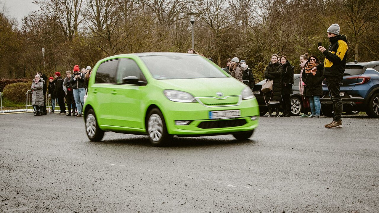 Grünes Elektroauto auf einem Parkplatz vor einer Menschengruppe