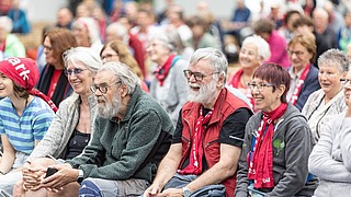 ublikum sitzt bei einer Podiumsveranstaltung und reagiert aufmerksam und fröhlich
