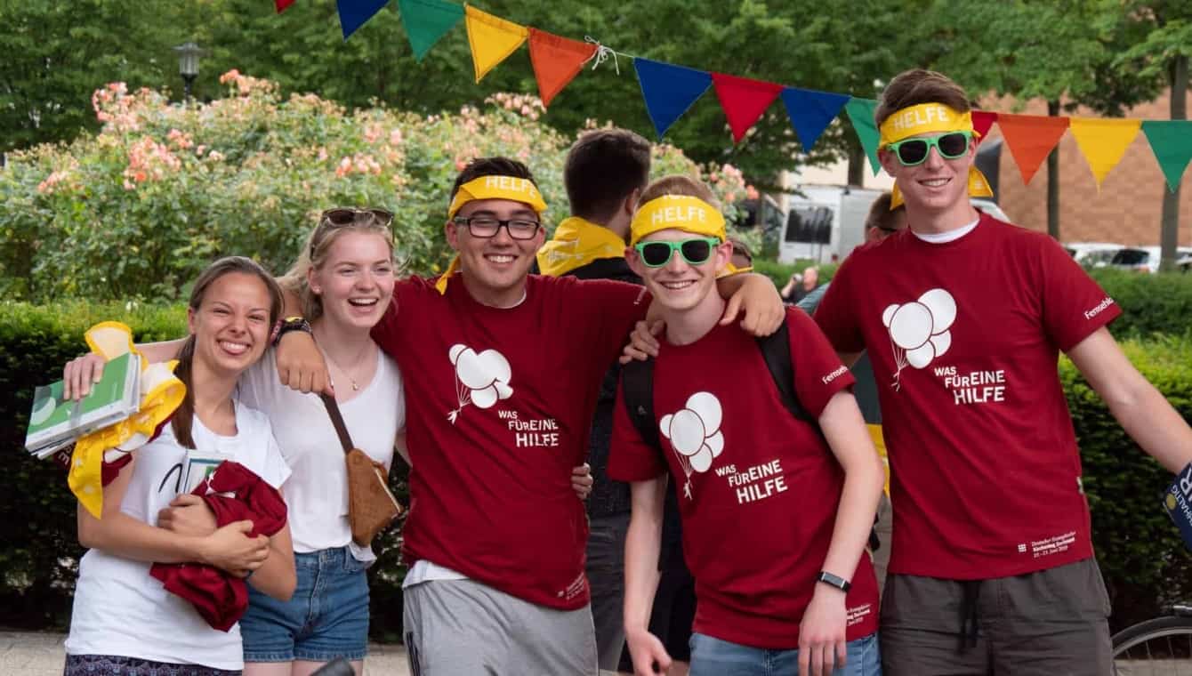 Helfer*innen beim Kirchentag in Dortmund (Foto: DEKT/FloGut) Jugendliche Helfende beim Kirchentag in Dortmund 2019 haben sich zum Gruppenfoto aufgestellt, 2 Mädchen im weißen Shirt und drei Jungen im roten Helfer-Shirt und mit dem gelben Helferhalstuch als Stirnband