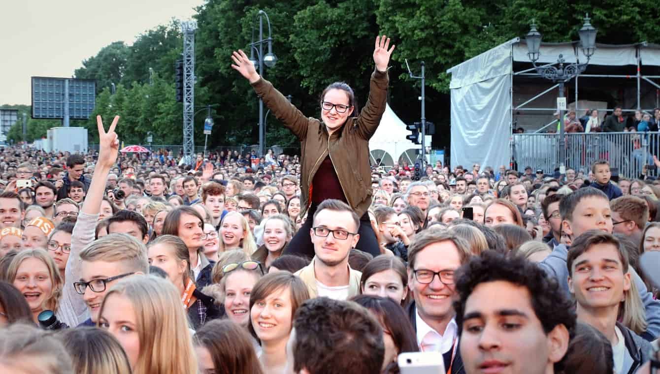 Konzertbesucherinnen beim Konzert von Max Giesinger, Abend der Begegnung in Berlin 2017. Ein Mädchen sitzt über der Menge auf den Schultern und streckt die Arme in den Himmel