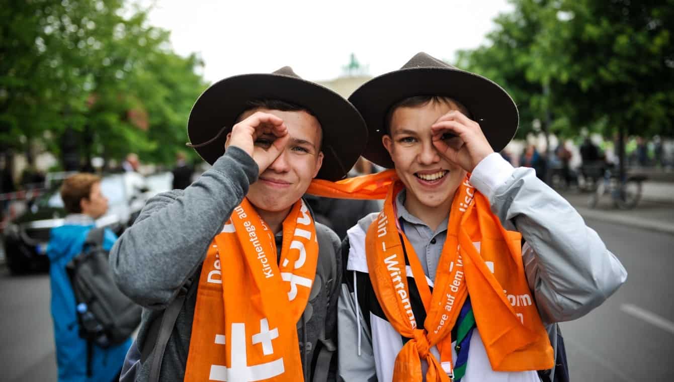 Zwei jugendliche Pfadfinder verspenden Schals beim Kirchentag in Berlin 2017 und formen das "Du siehst mich" Zeichen um die Augen