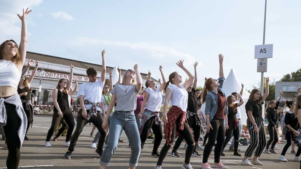 Jugendliche tanzen eine Choreographie und recken den linken Arm in den blauen Himmel beim Kirchentag 2019 in Dortmund 