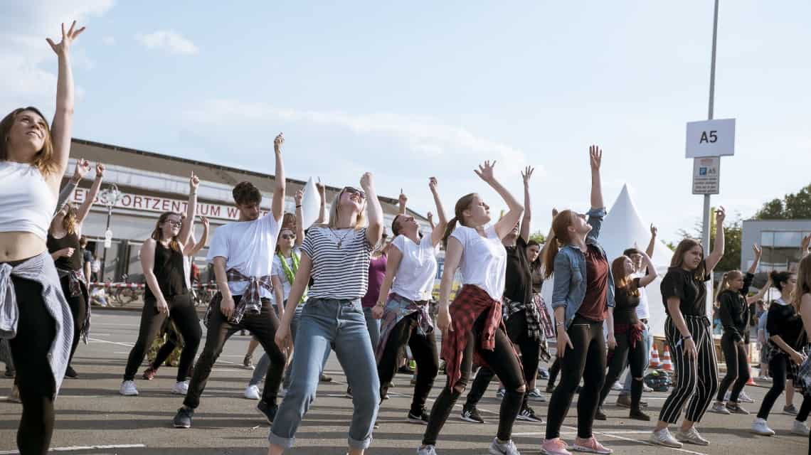 JJugendliche tanzen eine Choreographie und recken den linken Arm in den blauen Himmel beim Kirchentag 2019 in Dortmund 