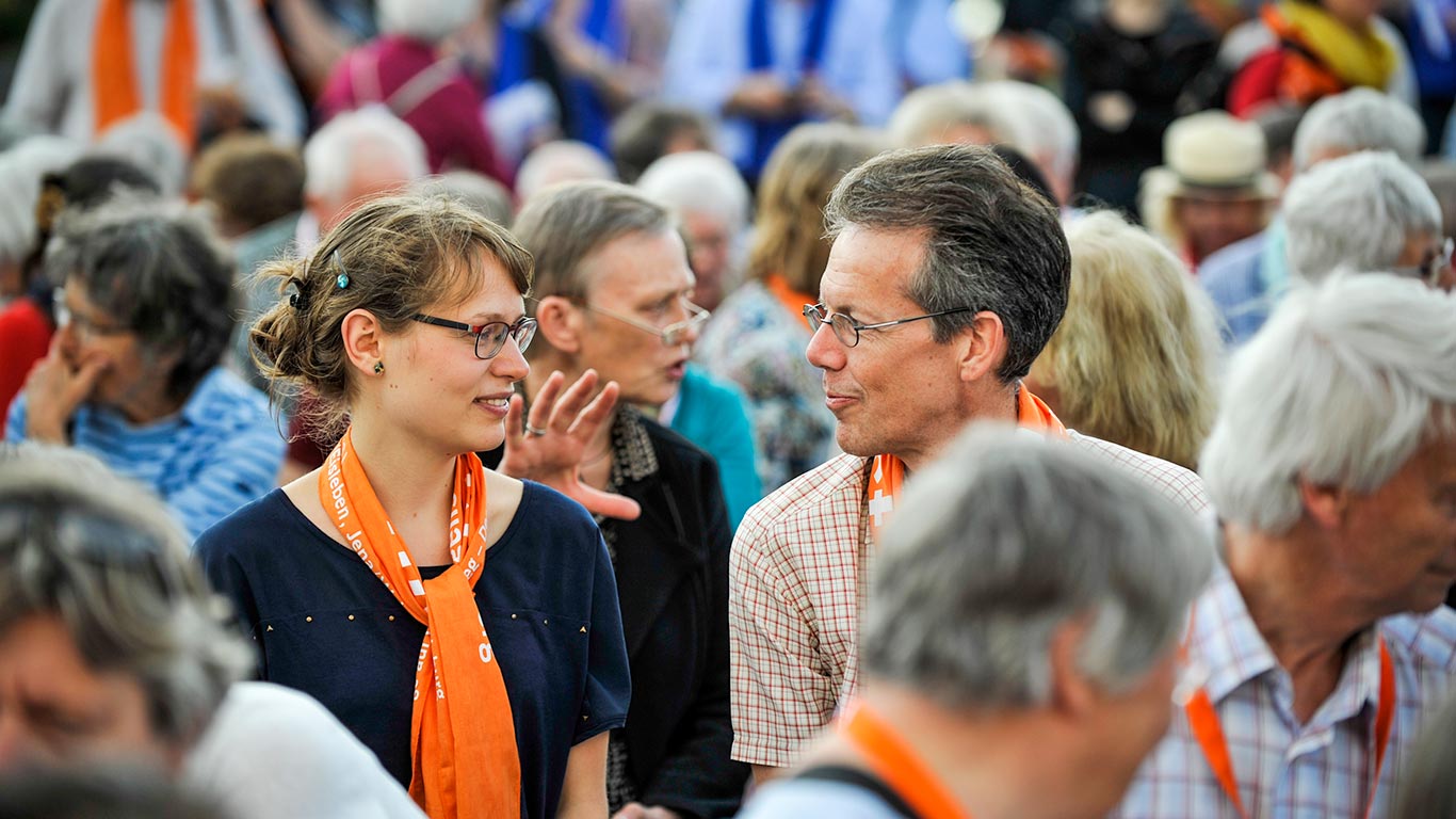 ein Mann und eine Frau sitzen in einer Menschenmenge und schauen sich an. Sie sind ins Gespräch vertieft