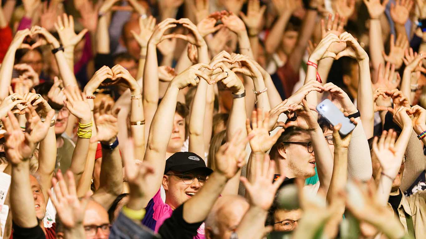 Teilnehmende beim Kirchentag in Hannover bilden während eines Konzerts Herzformen mit ihren Händen.