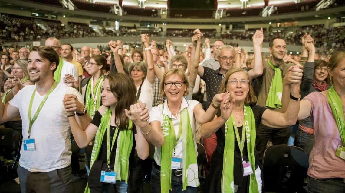 Teilnehmende beim Hauptpodium "Gemeinsam für offene Häfen in Europa" mit Leoluca Orlando. Sie stehen, halten sich an den nach oben gereckten Händen und lachen 