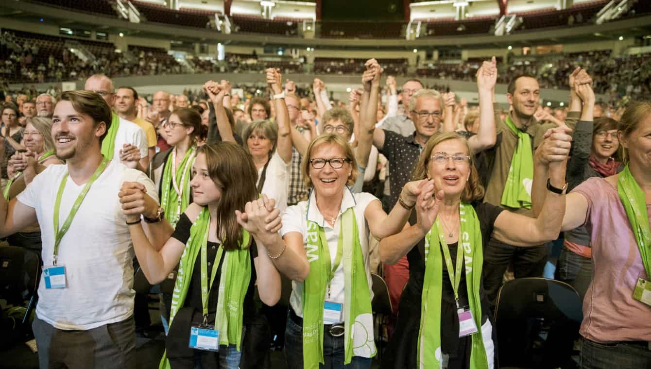 Teilnehmende beim Kirchentag in Dortmund 2019 Teilnehmende beim Hauptpodium "Gemeinsam für offene Häfen in Europa" mit Leoluca Orlando. Sie stehen, halten sich an den nach oben gereckten Händen und lachen