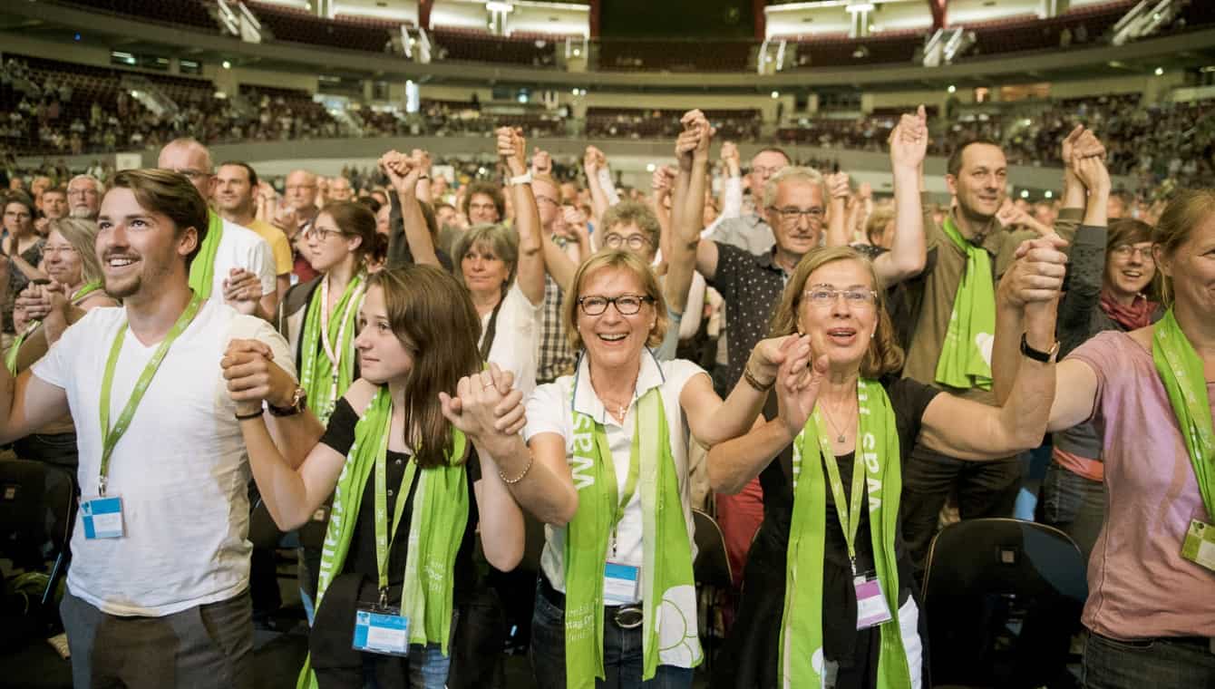 Teilnehmende beim Hauptpodium "Gemeinsam für offene Häfen in Europa" mit Leoluca Orlando. Sie stehen, halten sich an den nach oben gereckten Händen und lachen 