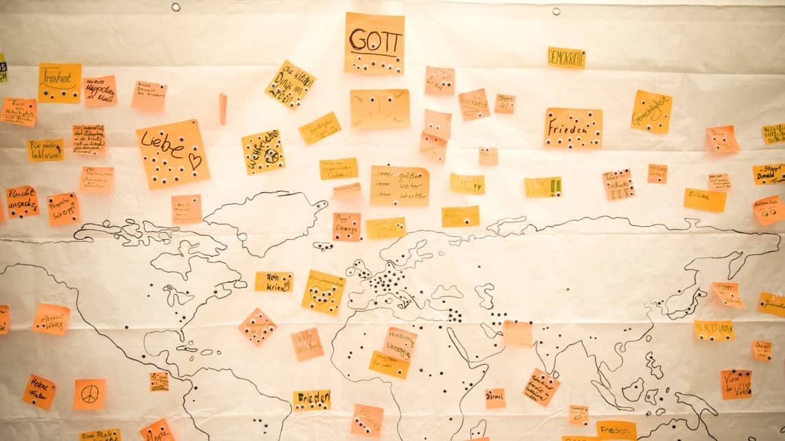 Pinnwand mit orangenen Klebezetteln auf einer Weltkarte im Zentrum Jugend Kirchentag Berlin 2017