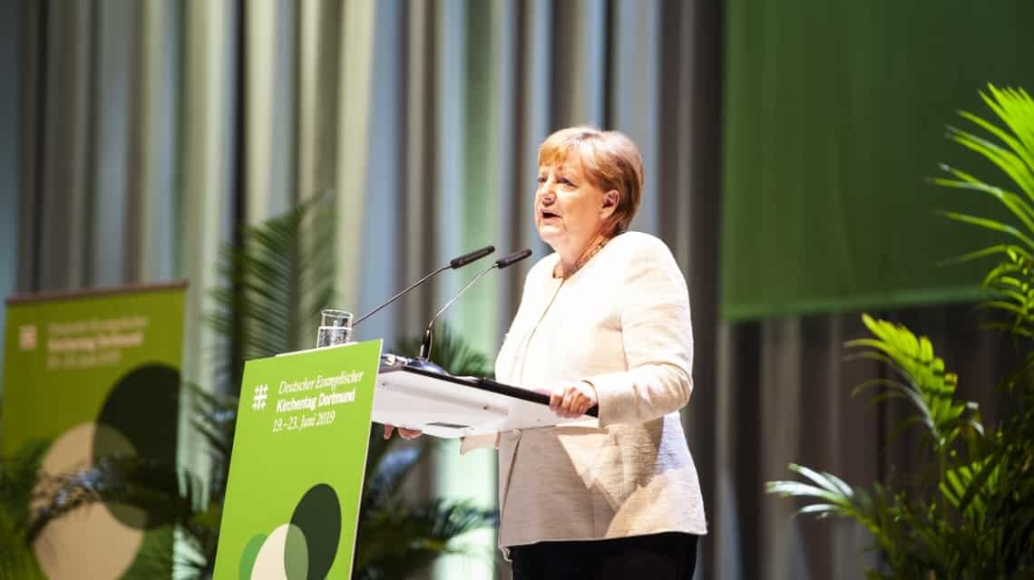Angela Merkel beim Hauptvortrag "Vertrauen als Grundlage internationaler Politik?" Sie steht am Rednerpult und trägt einen cremefarbenen Blazer