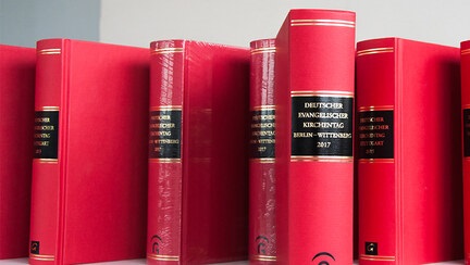 Mehrere rote Dokumentarbände (dicke Hardcoverbücher) vergangener Kirchentage