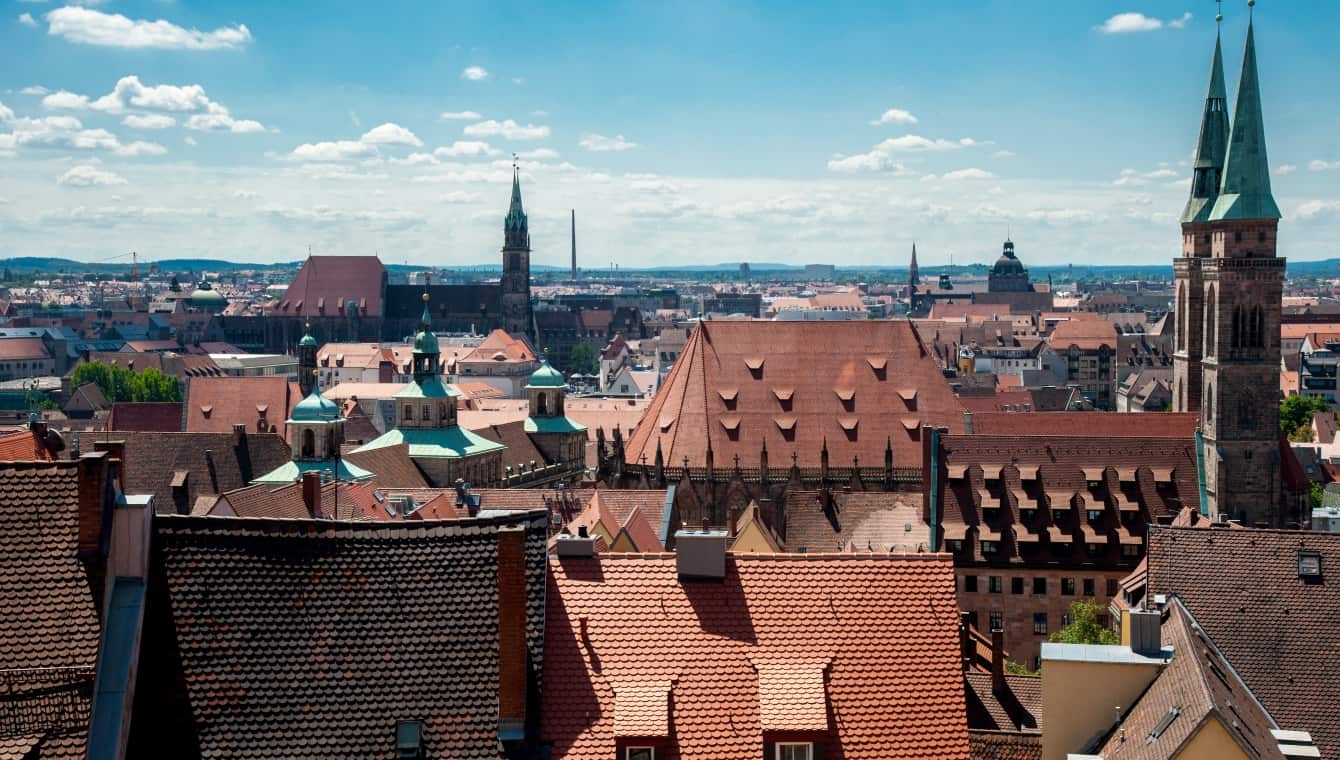 Blick über die Dächer der Innenstadt von Nürnberg, die Kirchtürme von St. Sebald rechts im Bild und St Lorenz weiter hinten sind zu sehen, blauer Himmel mit Schäfchenwolken