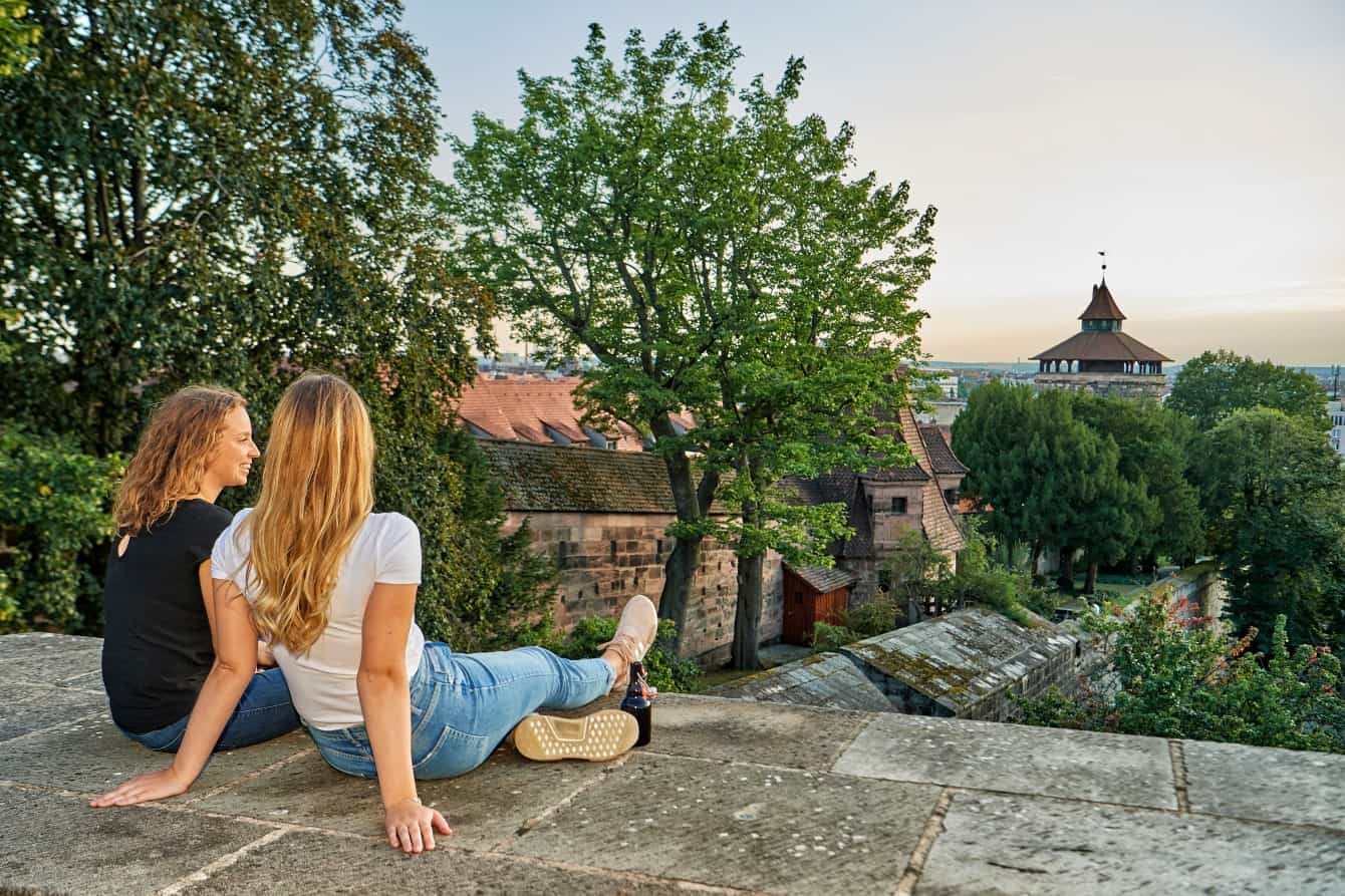 Zwei junge Frauen sitzen auf der Mauer der Kaiserburg und schauen über die Burgmauern auf die Stadt