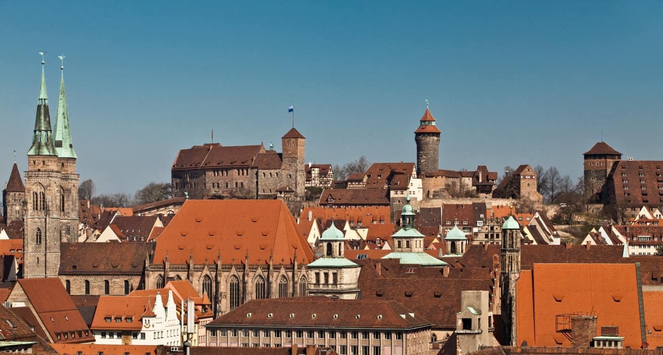 Blick über die Nürnberger Altstadt bei blauem Himmel, links die Türme und die Kirche St. Sebald, mittig hinten die Kaiserburg