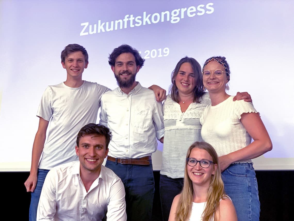 Jugendausschuss 2019 Gruppenfoto: Kevin Beier, Jakob Güntter, Nina Kruschewski, Richard Lange, Katharina Matthias, Eva Seibold und Kira Stütz. Alle tragen weiße Oberteile und stehen vor eine Fliederfarbenen Rückwand auf der "Zukunftskongress 2019" steht