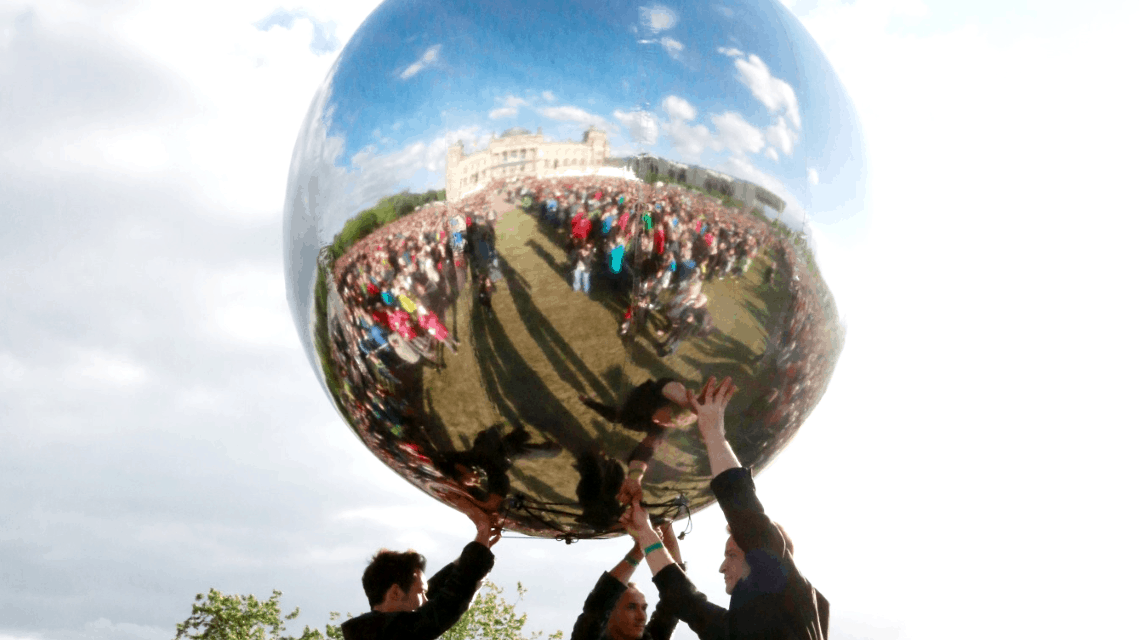 Performance mit einem riesigen silbernen Ball in dem sich die Zuschauermenge und der Reichstag spiegeln, drei schwarz gekleidete Männer recken ihn in die Höhe