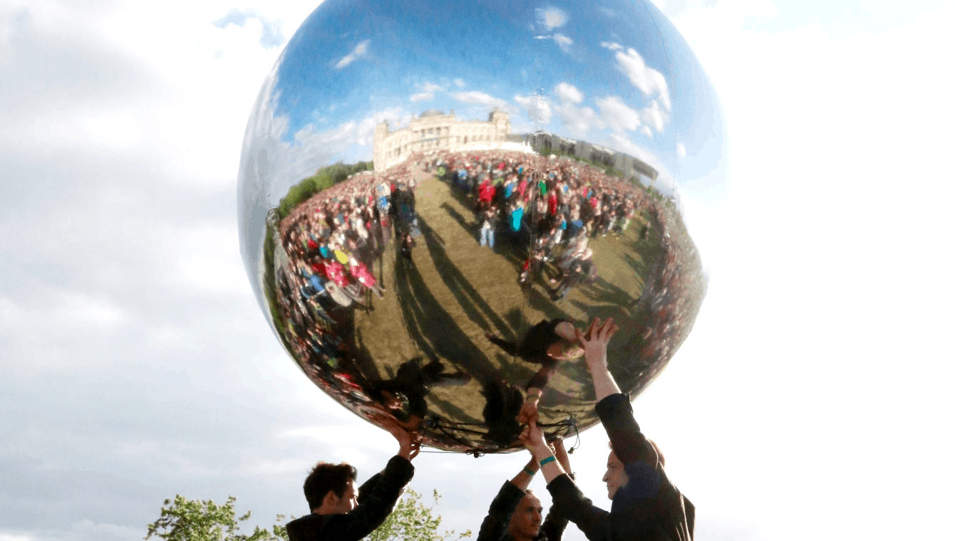 Performance mit einem riesigen silbernen Ball in dem sich die Zuschauermenge und der Reichstag spiegeln, drei schwarz gekleidete Männer recken ihn in die Höhe