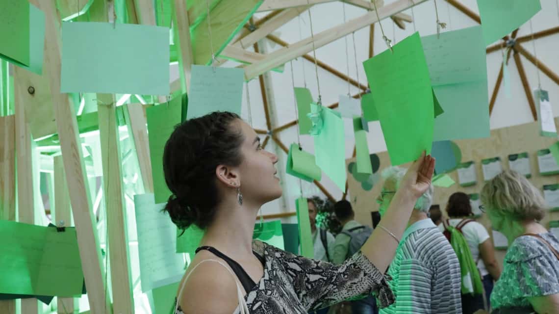 Teilnehmerin liest gute Nachrichten hinterlassen auf grünen Zetteln, die überall im Raum hängen, von anderen Teilnehmenden im Pavillon der guten Nachrichten auf dem Kirchentag in Dortmund