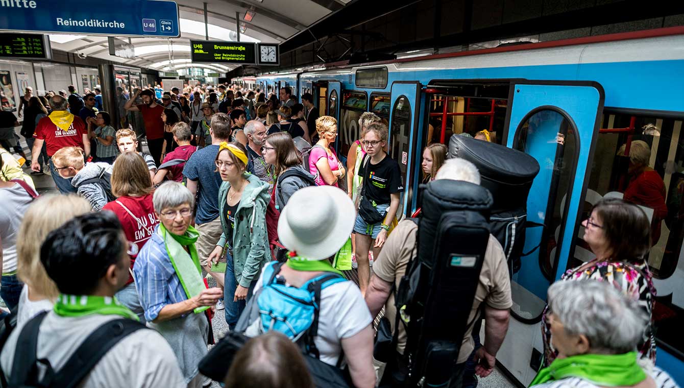 Menschenmenge in U-Bahnstation. Auf der rechten Seite steht ein Zug. Die Menschen tragen den grünen Kirchentagsschal